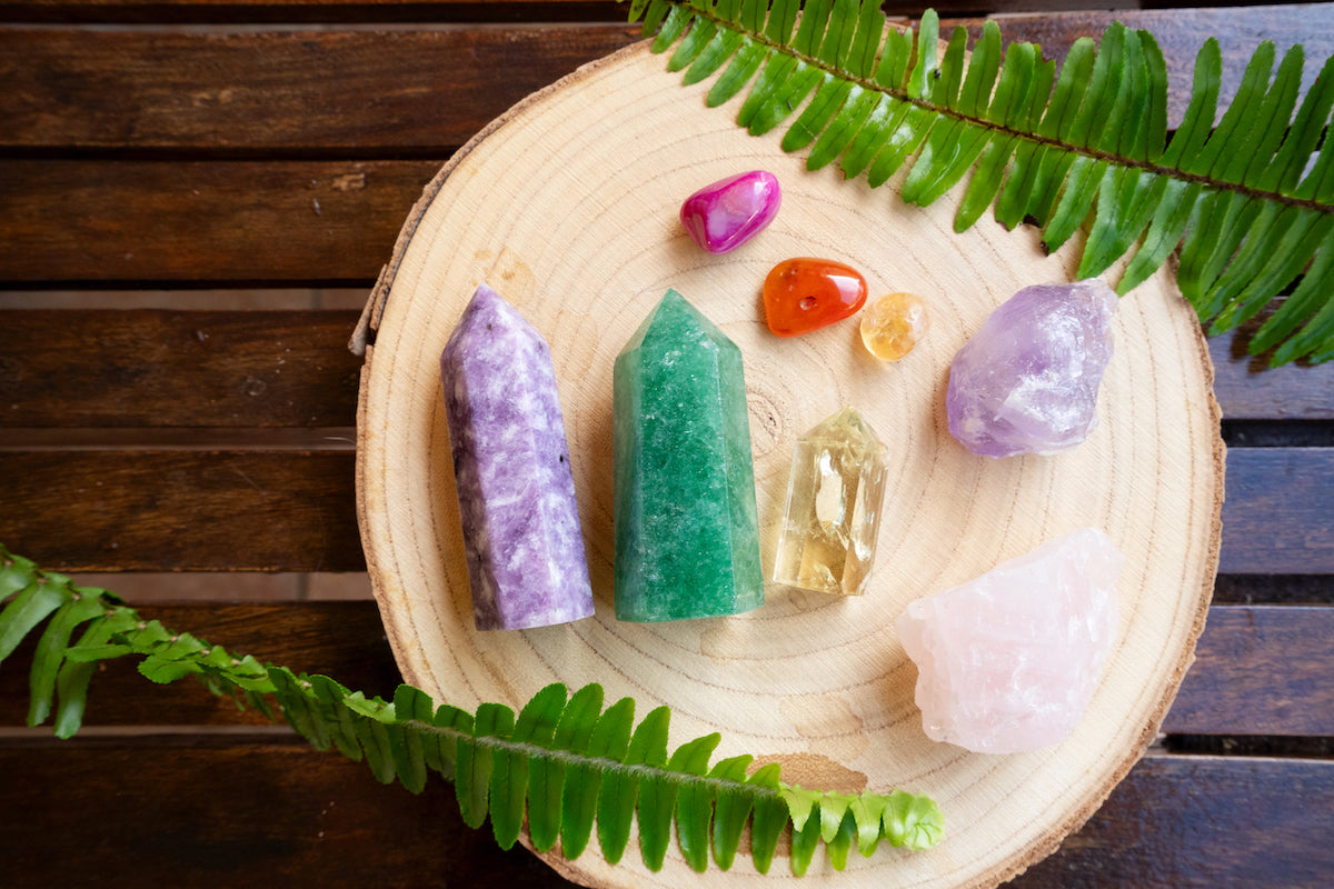 Crystals collection banner for The Tiny Topaz showing colourful crystals on a wooden board with surrounding green plants.