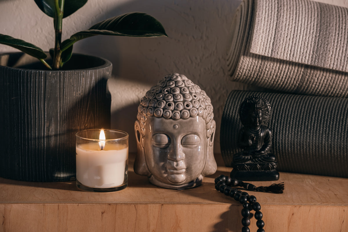 Home decor collection banner for The Tiny Topaz showing a Buddha head ornament, next to a lit candle and a plant.