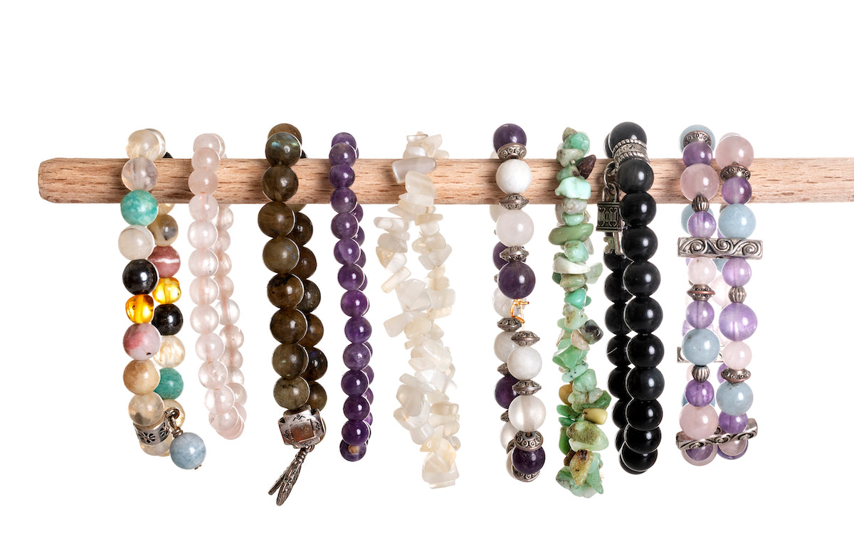 Jewellery collection banner for The Tiny Topaz showing multiple colourful crystal bracelets hanging in a row on a wooden pole.