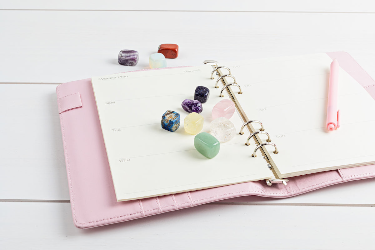 Journals and Notebooks collection banner for The Tiny Topaz showing colourful tumblestone crystals on a pink calendar diary with pen..