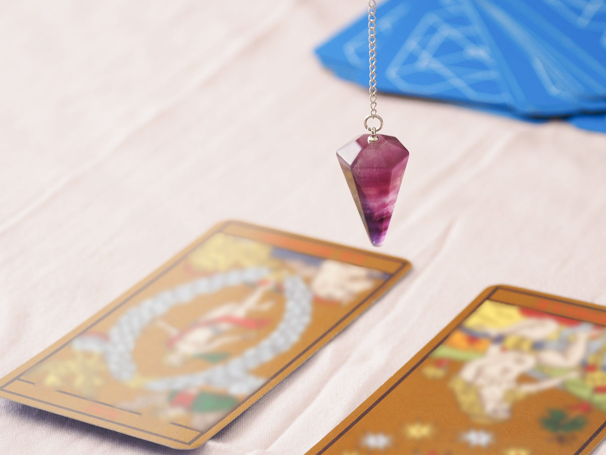 Tarot cards collection banner for The Tiny Topaz showing a purple crystal drop necklace dangling over tarot cards laid down on the table.