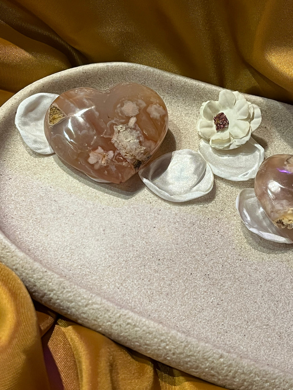 Heart shaped flower agate on a stone plate with flowers and flower petals on a gold background